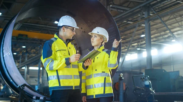 在硬帽的男性和女性工业工程师在使用平板电脑时讨论新项目 他们在重工业制造厂工作 — 图库照片