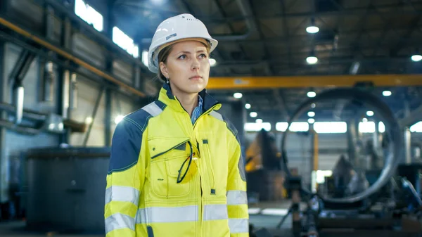 硬帽中的女性产业工人站在重工业制造工厂的中间 在背景中看到了各种金属制品组件 — 图库照片