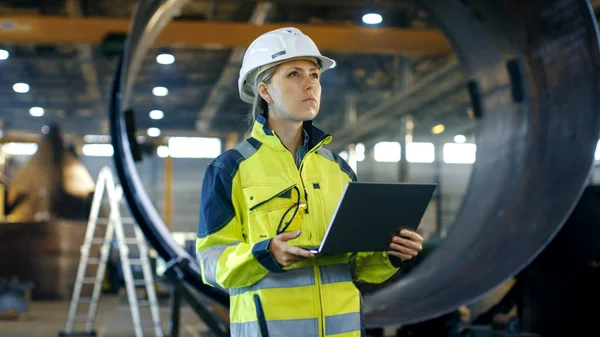 在重型工业制造厂 硬帽的女工业工程师使用笔记本电脑 在背景下各种金属制品工程零件的谎言 — 图库照片