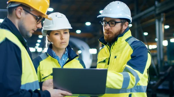 男性和女性工业工程师在使用笔记本电脑时与工厂工人交谈 他们在重工业制造工厂工作 — 图库照片