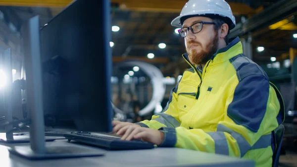 工业工程师在个人计算机工作区工作 他穿着安全帽和安全夹克 在重工业制造厂的主要车间工作 — 图库照片