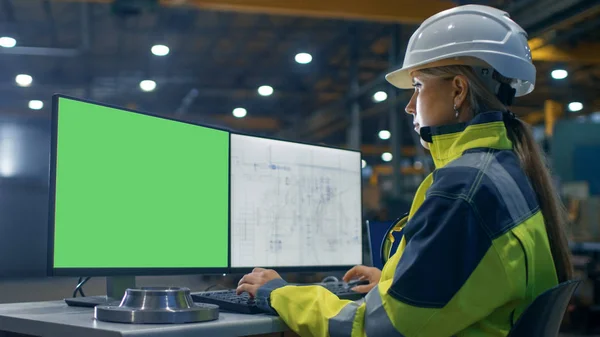 Inside the Heavy Industry Factory Female Industrial Engineer Works on the Personal Computer with Green Mock-up Screen. Secondary Monitor Shows Blueprints.