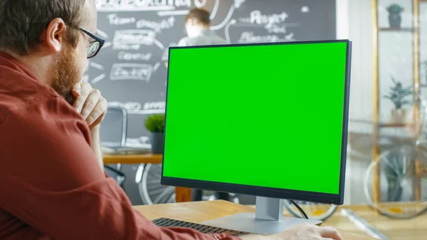 人在个人电脑上工作 绿色的模拟屏幕 在背景创意办公室与人画黑板墙 — 图库照片