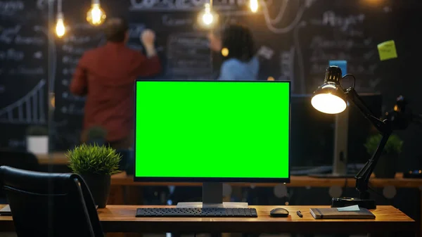个人电脑与模拟绿色屏幕显示器站在办公桌上 在后台的人工作在黑板墙在创意办公室 — 图库照片