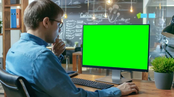 年轻人在他的办公桌上工作在个人电脑与模拟绿色屏幕 在后台 他的同事在创意办公室工作 — 图库照片