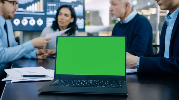 会议桌上带绿色色度键屏幕的会议室笔记本电脑 在后台业务人员有重要的讨论 — 图库照片