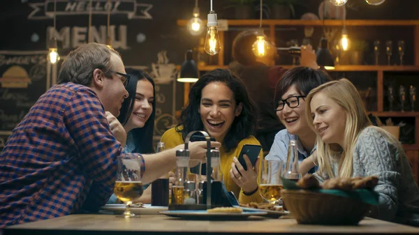 美丽的拉美裔妇女显示有趣的东西 她的智能手机上她的朋友 而他们有良好的时间在酒吧 他们笑 喝在时尚的时髦酒吧建立 — 图库照片