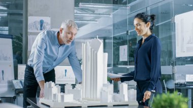 Mimari büro kadın mühendis getiriyor planlar içinde ve kıdemli mimar, onlar tartışmak proje gösterir. Bir yapı modeli kentsel planlamacılar çalışıyorlar.