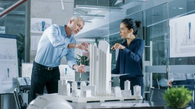 İki profesyonel erkek ve dişi mimari mühendis iş planları ve yapı modeli tasarımı üzerinde kentsel planlama Project.Clean minimalist Ofis için beton duvarlar planları ve belgeler.