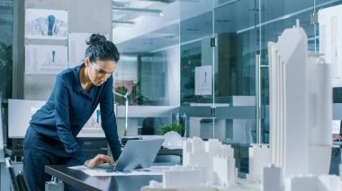 Kadın mimari Tasarımcısı, yeni bina modeli için kentsel tasarım projesi mühendislik bir dizüstü bilgisayarda çalışır. Temiz minimalist Office, beton duvarlar planları ve belgeler.