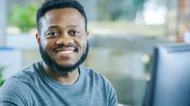 Bir kişisel bilgisayar üzerinde genç siyah adam çalışır tatlı kamerada gülümsüyor. Kesilmiş sakallı şık akıllı adam.