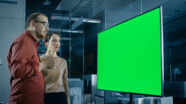 Erkek ve kadın iş arkadaşları konferans salonunda bir sunum TV'de gösterilen yeşil ekran Chroma anahtar şablon hakkında tartışma var.