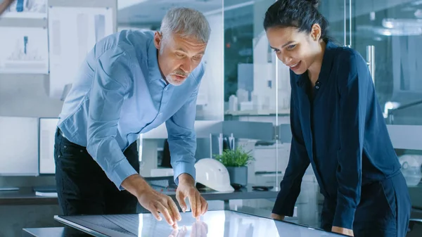 高级男性和年轻女建筑设计师在图形平板电脑上绘制建筑概念显示垂直触摸屏表 它们使用手势缩放项目模型 — 图库照片