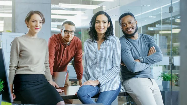 Portrait Shot of a Diverse Group of Talented Young Professionals Sitting on a Desk in the Stylish Modern Environment. Real People Sincerely Smiling on Camera.
