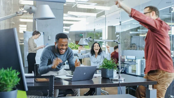 Busy Corporate Office, Man Working on a Laptop Signs Important Contract and Jumps in Celebration, Gives High-Five to His Coworkers. Everybody is Happy.