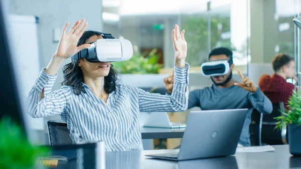 Female Virtual Reality Engineer/ Developer Wearing Virtual Reality Headset Creates Content With Her Colleagues. Bright Young People Work on the Augmented & Mixed Reality Project.