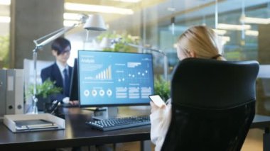 Office çekici kadın sandalye, gülümsüyor ve kullandığı cep telefonu Swirles. Onun masaüstü bilgisayar ekranı Infographics onun şirketin hisselerinin istatistiksel büyüme ile gösterir. Stylish Room ortamda güzel kadın.
