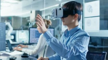 Bilgisayar bilim mühendisi sanal gerçeklik kulaklık inşaat ile 3d modelleme, jestler yapar giyiyor. Arka plan mühendislik bürosu ile meşgul arkadaşlarıyla.