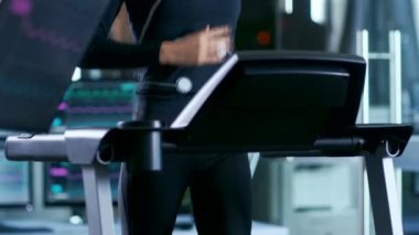 Cesedin yanına bağlı elektrotlar ile güzel bir kadın sporcu spor bilim laboratuarında bir koşu bandı üzerinde çalışır. Arka plan yüksek teknoloji laboratuvar monitör ile Ekg okuma gösterilen.