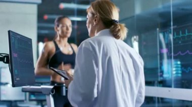 Güzel kadın atlet çalışır onun vücut bağlı elektrotlar ile bir koşu bandı üzerinde kadın hekim Touchscreen ile etkileşim ve laboratuvar kontrolleri Ekg verileri gösteren izler.