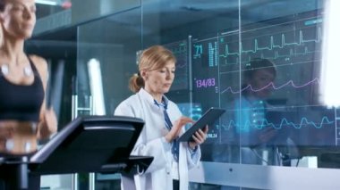 Güzel kadın atlet çalışır onun vücut bağlı elektrotlar ile bir koşu bandı üzerinde kadın hekim Tablet bilgisayar kullanır ve Ekg Laboratuvarı monitörde gösterilen veri denetimleri.