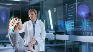 Kadın giyiyor Brainwave tarama kulaklık oturur bilim adamı ayarlar ise bir sandalyede cihaz görünüyor görüntüler. Modern beyin çalışma laboratuvar monitör Haritayı Eeg okuma ve beyin modeli.