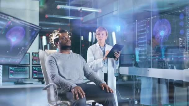 男を着て脳波スキャン ヘッドセットに座ってながらタブレット コンピューター監督プロセスの科学者の椅子 現代脳研究所モニターを脳波読書と脳のモデル — ストック動画