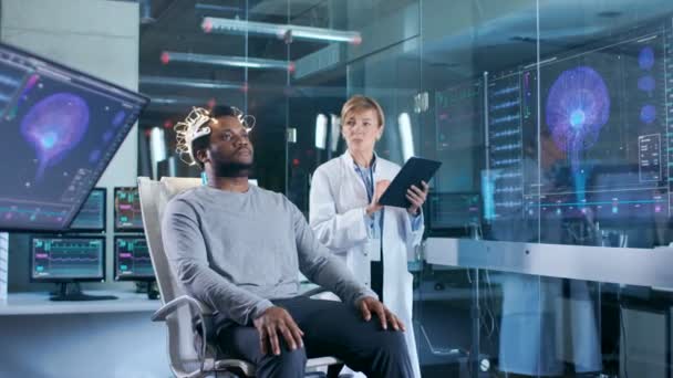 男を着て脳波スキャン ヘッドセットに座ってながらタブレット コンピューター監督プロセスの科学者の椅子 現代脳研究所モニターを脳波読書と脳のモデル — ストック動画