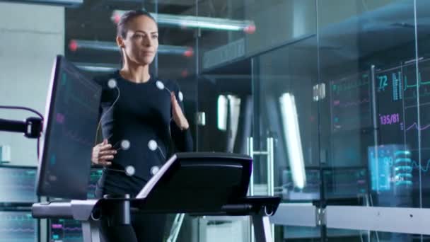 在科学体育实验室美丽的女运动员运行在跑步机上与电极连接到她的身体 监视器显示 Ekg 数据在显示 慢动作 — 图库视频影像