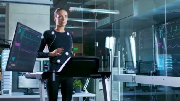 in wissenschaftlichen Sportlabor schöne Sportlerin läuft auf einem Laufband mit Elektroden an ihrem Körper befestigt, Monitore zeigen ekg-Daten auf dem Display. Zeitlupe.