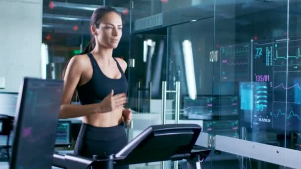 在科学体育实验室美丽的女运动员走在跑步机上与电极连接到她的身体 显示器显示 Ekg 数据在显示 慢动作 — 图库视频影像