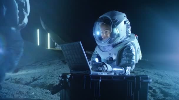 新しく探索 ノート パソコンで宇宙服の作品を着ての女性宇宙飛行士は 地球との通信を発見しました バック グラウンドで彼女の乗組員のメンバーとスペース生息地 植民地化の概念 — ストック動画