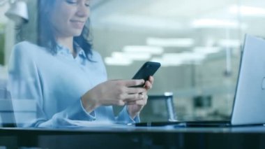Güzel kadın ofis işçi kullanır dizüstü bilgisayar ile çalışan Her masada oturma sırasında Smartphone. Modern cam ve beton Oda.