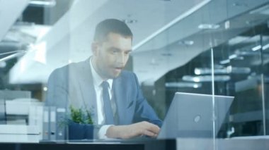 Gergin işadamı bir dizüstü bilgisayarda masasında iş sorunlarını çözmeye çalışıyor. Modern cam ofis şık adam.