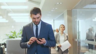 Cep telefonu kullaranarak odaklı iş adamı meşgul kurumsal yapı koridor yürüyor. Çok sayıda farklı iş halkların kendi iş hakkında gitmek.