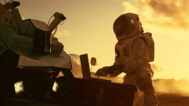 Astronot uzay giysisi içinde çalışır Rover bir yeni yabancı kırmızı gezegende ayarlama bir dizüstü bilgisayarda / Mars. Gün ışık yüksek teknolojili uzay araştırmaları, yaşanabilir gezegenlerin, kolonizasyon keşfi.