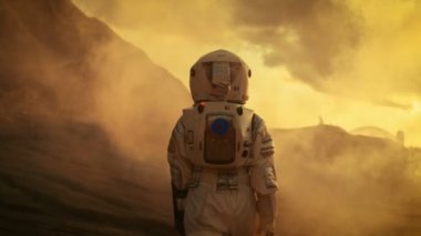 Aşağıdaki Shot güvenle Mars, Turing çevresinde ve kameraya bakarak yürüyüş alanı elbiseli kadın astronot. Kızıl gezegen gaz ve duman kaplı.