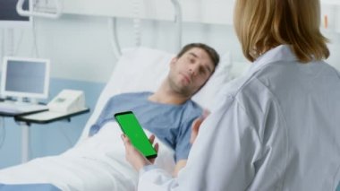 Profesyonel erkek doktor görüşmeleri ile yatakta yatan hasta sapık, o yeşil ekran cep telefonu kullanır. Tıbbi teknoloji.