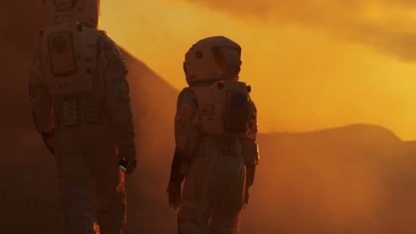 つの宇宙飛行士が宇宙服を着ての背面図歩く火星探査 赤い惑星 宇宙旅行 植民地化の概念 — ストック動画