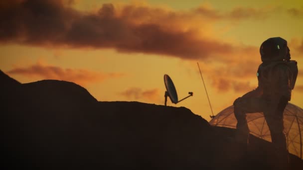 エイリアンの赤い惑星の岩山の上に立って宇宙飛行士のシルエット 火星します 火星に最初の有人宇宙飛行 ベースと背景の夕焼け 駅を研究 — ストック動画