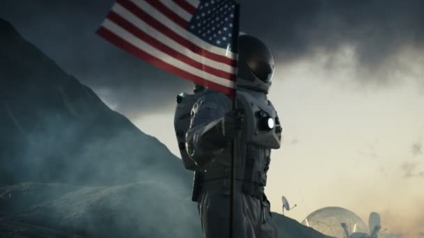 旗が付いている強力な宇宙飛行士歩行暗いエイリアンの惑星上のアメリカの状態を結合します 宇宙旅行 植民地化のテーマ — ストック動画