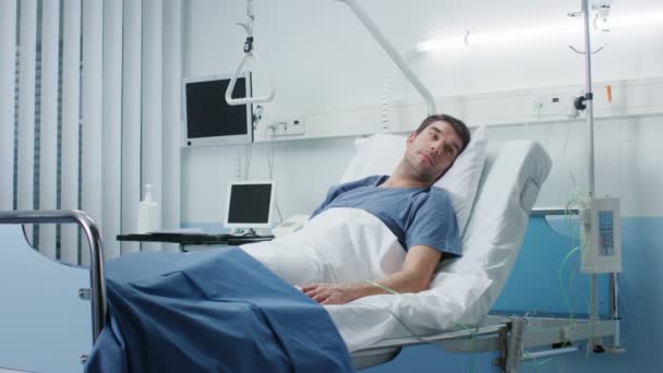 真剣に病気男が病院のベッドの上に横たわる 彼のバイタル サインをモニターに表示します 病棟はクリーンと新しい — ストック動画
