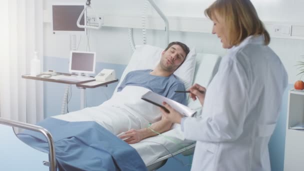 プロフェッショナル女性医師訪問の男性患者 記入カルテにタブレット コンピューターを使用して 彼女は質問を求めてベッドに横たわっています 患者に優しい医療医師笑顔 — ストック動画