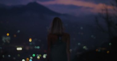 Arkadan görünüm atış silah ile gece yetiştirme / şehir akşam genç bir kadın silueti ışıklar ve dağ tepeleri içinde belgili tanımlık geçmiş.