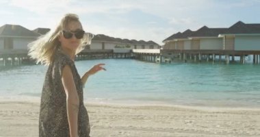 Güzel sarışın kadın için Come davet Beach üzerinde çalışan. Overwater / yüzer bungalovlar ve villalar kıyıdan gördün. Güzel doğa.