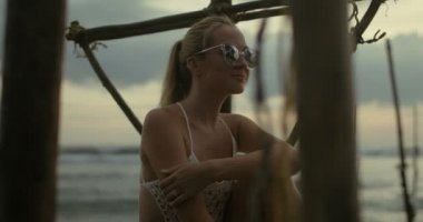 Ağır çekim Shot mayo ve güneş gözlüğü balıkçılık Uzunbacak üzerinde oturan güzel sarışın. Arka plan deniz ve doğa.