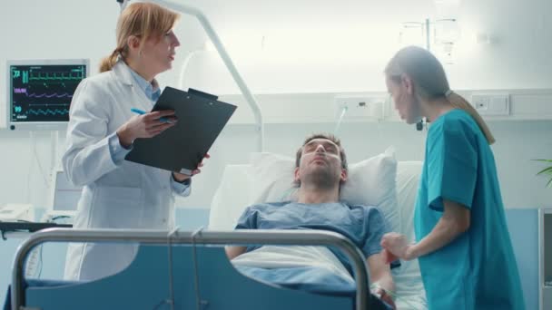 在医院生病的男性患者躺在床上 专业的女医生写在病人的图表 地址护士谁检查下降柜台和增加剂量的疼痛杀手 — 图库视频影像