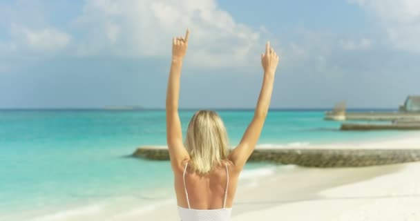 美丽的金发碧眼的女人的肖像戴太阳镜摆姿势和微笑在海滩上 举起武器 她在背景海度假村快乐 — 图库视频影像