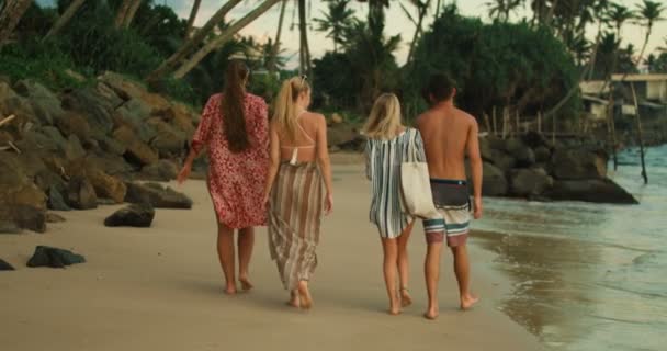 后拍摄的三个美丽的女孩和一个英俊的男人走在海滩上 可爱的绿色森林与棕榈树在他们之前 — 图库视频影像