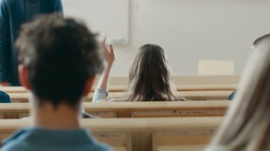 Arkadan Görünüş konferans salonunun öğrencilerin, ders veren bir Profesör dinleme, bir öğrenci el yükseltir ve soru soran.